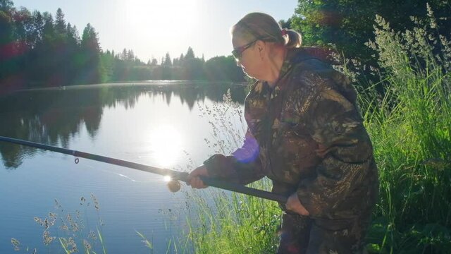 Woman fishing. Elderly angler woman fishing on the calm summer pond during sunset