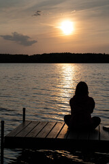 Silhouette of girl sitting alone on dock facing sunset