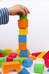 A child builds a pyramid of cubes on a white background. The boy's hand holds a cube.