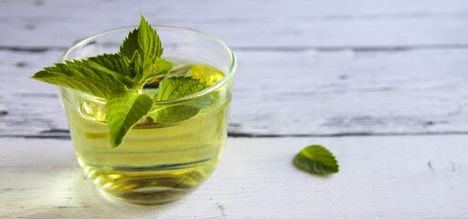 Fresh mint tea concept on a wooden background. Mint tea in a transparent cup and one mint leaf on the table. Banner.