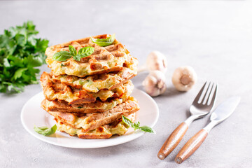 Zucchini waffle, zucchini fritters cooking on waffle maker, vegetarian zucchini waffles with basil and garlic in a plate on a light background