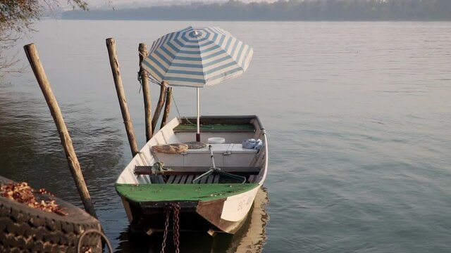 Small wooden fishing boad with umbrella tied up to a river shore