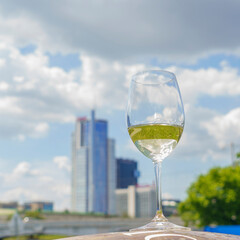 Glass of white wine with reflection on the blurred cityscape and dramatic sky background. Space for text. Wine concept.