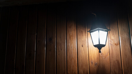 Glowing street lamp on the background of a wooden wall at night. Light permeates the darkness. Street lighting. Creating a cozy. Space for text.