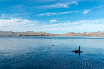 Obraz premium landscape of a calm sea, with mountains in the background, and a cormorant resting on a floating platform
