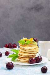 Breakfast with a cup of coffee and a stack of classic american pancakes served with black cherry, apricot, kiwi and mint. Blue stone background.
