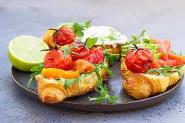Variety of croissant sandwiches with grilled pepper, tomatoes, smoked salmon, turkey, avocado and arugula served with micro green on grey concrete background.