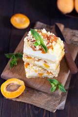 Delicious raw apricot cheesecake with crumble on wooden cutting board, dark background. Healthy vegan food concept.