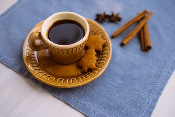 A cup of coffee and a delicious Christmas cookie lies on a blue linen napkin on a white table.