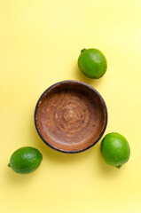 Fresh juicy limes around an empty brown clay plate on a yellow background. citrus vitamin C healthy...
