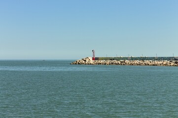 The pier of Pesaro harbor with breakwater cliffs, a colored wall and a small red lighthouse (Marche, Italy, Europe)