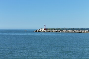 The pier of Pesaro harbor with breakwater cliffs, a colored wall and a small red lighthouse (Marche, Italy, Europe)