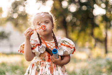 A girl with Down syndrome blows bubbles. The daily life of a child with disabilities. Chromosomal...