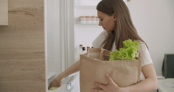 woman unpacking food bag into fridge