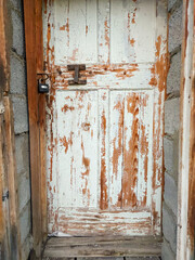 Old wooden door in field stone wall with rusty hinges and padlock