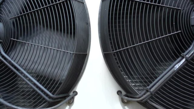 Tilting shot of two large industrial air conditioning condenser fans slowly rotating