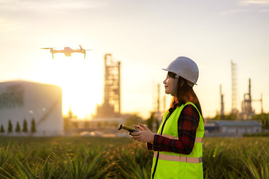 Asian woman engineer operate flying drone over oil refinery plant during sunrise building site survey in civil engineering project.