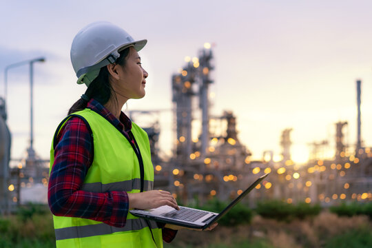 Asian woman petrochemical engineer working at night with laptop Inside oil and gas refinery plant industry factory at night for inspector safety quality control..