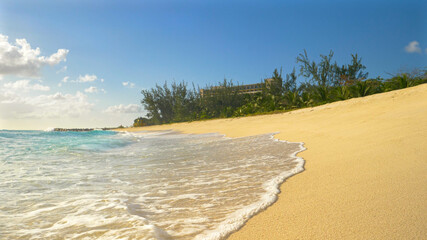 Obraz premium LOW ANGLE: Glassy ocean waves wash the white sand beach on a sunny evening.
