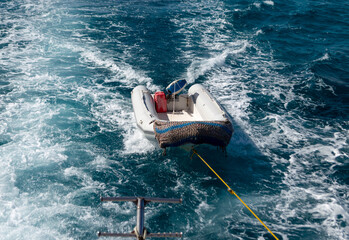 Rescue inflatable boat tied to sightseeing yacht on the waves in the trail of yacht on the water