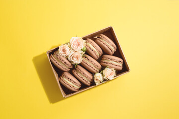 Many chocolate macarons in craft box with roses on the yellow background.
