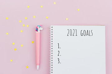 Diary for setting goals for 2021 and unicorn pen on pink background decorated golden confetti. New Year's resolution. Flat lay, top view