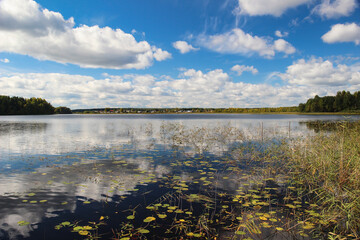 Beautiful landscape. Clouds over the lake reflecting in water and village on the horizon.