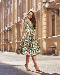 Beautiful brunette young woman wearing stylish sunglasses, colorful green midi dress and high heels...