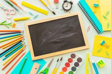School supplies stationery, colour pencils, paints, alarm clock on light blue background. Back to school concept, mock up