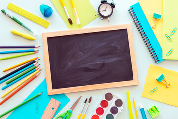 School supplies stationery, colour pencils, paints and alarm clock. Blackboard with space for text. Back to school concept