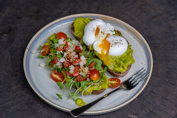 Healthy breakfast with bread toast and poached egg with green salad, red tomato and smashed avocado