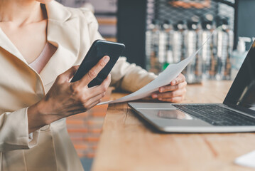 Business woman working on smart phone and laptop searching web, browsing information sitting doing work at desk