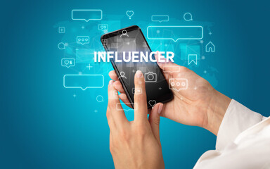 Female hand typing on smartphone with INFLUENCER inscription, social media concept