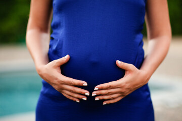 Women's hands hug pregnant belly in blue dress