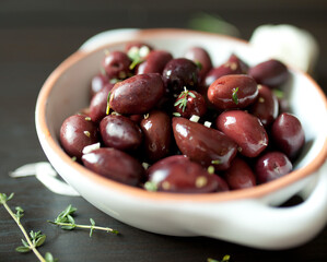 Seasoned kalamata olives in white dish with herbs on dark background