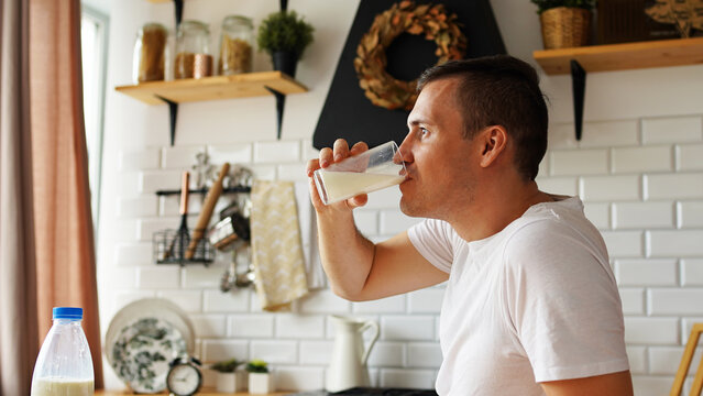 Young man drinking milk in kitchen. Adult male enjoying useful drink for breakfast.