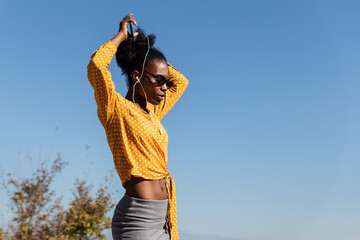 young beautiful black woman enjoying nature while listening to music and dancing