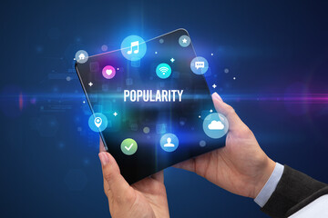Fototapeta premium Businessman holding a foldable smartphone with POPULARITY inscription, social media concept