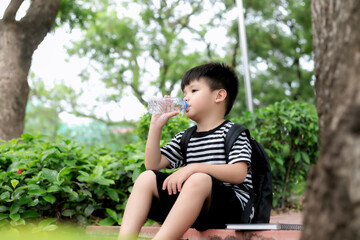 Cute little boy drinking mineral water from the plastic bottle in the park