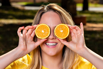 Happy and smiling young woman playing with an orange cut in half and in front of her eyes. Photo in...