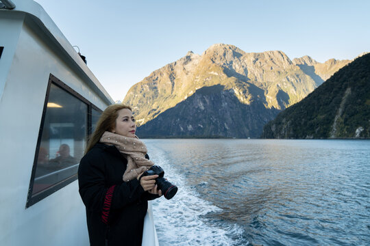 Asian woman taking picture with beautiful scenic of milford sound in fiordland national park new zealand.