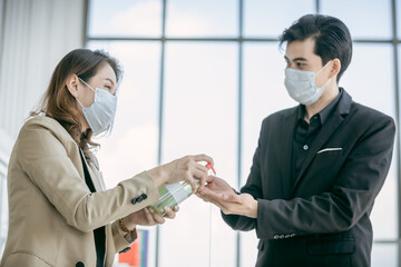Fototapeta premium Business woman to share alcohol gel to business man at the office to protect covid-19 coronavirus.Social and business distancing new normal lifestyle.