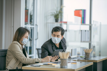 Business office working together at new normal social distance with table shield partition reduce infection of coronavirus covid-19 pandemic. Social and business distancing new normal lifestyle.
