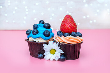 sweet dessert two cream cupcakes decorated with large berries strawberries and blueberries and flowers on a pink background with white glowing lights