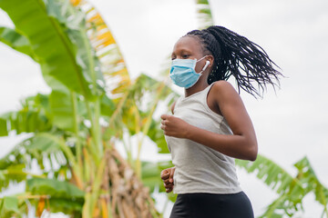 post quarantine runner girl enjoying outdoors workout - young attractive and fit black African American woman running wearing face mask in new normal sport practice