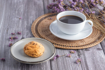 Close-up of a cookie on a plate with a white coffee cup and flower blurred background