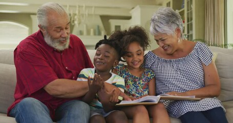 Grandparents and grandchildren reading book at home - Powered by Adobe