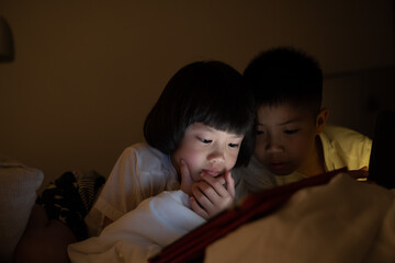 Obraz na płótnie Canvas two chinese children addicted tablet, asian child watching telephone together on their bed, kid using smartphone 