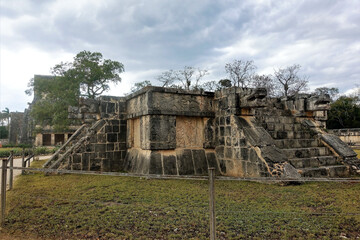 The ancient Mayan city of Chichen Itza. Platform Jaguars and Eagles. A square stone pedestal with stairs and snake heads upstairs. On the walls carved drawings of jaguars and eagles. Cloudy sky.  