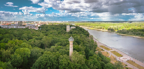 City panorama public park with a large green area near the river an old lighthouse in the trees a blue sky with cumulus clouds on the landscape. Aerial view